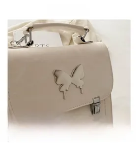 Close-up of cream shoulder bag with large silver butterfly and dual metal buckles