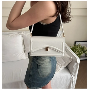 Detail of white leather shoulder bag featuring gold buckle and refined stitching on flap