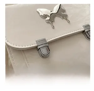 Detail of matte cream leather bag featuring silver butterfly ornament and metal buckles