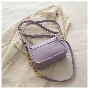 Dettaglio della borsa a tracolla rettangolare viola chiaro con catena d'oro su blazer crema