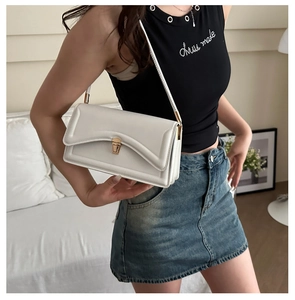 Detail of a creamy white shoulder bag featuring a gold clasp and V-shaped stitching