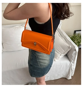 Detail of a bright orange baguette bag with a silver metal buckle and glossy finish