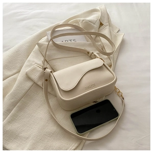 Détail du sac bandoulière blanc crème avec rabat ondulé sur un blazer texturé
