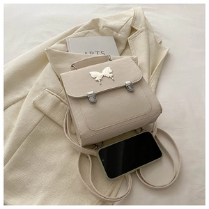 Detail of a cream faux leather backpack featuring a large metal butterfly clasp and straps