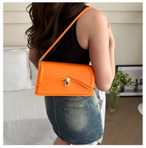 Detail of bright orange rectangular shoulder bag with golden clasp and matte texture