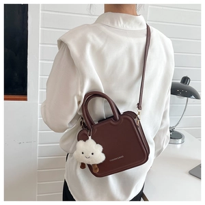 Detail of dark brown faux leather crossbody bag with cloud plush pendant and shoulder strap