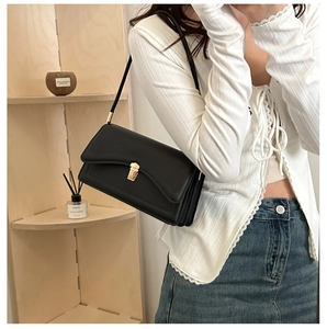 Minimalist black leather underarm bag with gold lock hardware on a female model