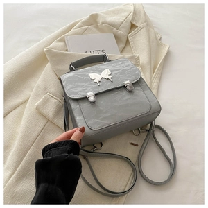 Detail of grey pleated leather backpack featuring a silver butterfly charm and slim straps