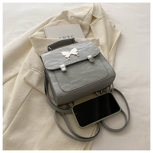 Detail of grey glossy leather backpack with butterfly buckle and smartphone for scale