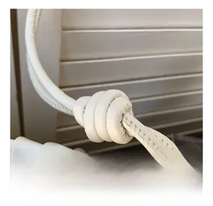 Detail of white leather shoulder bag with knotted strap design and gold zipper closure