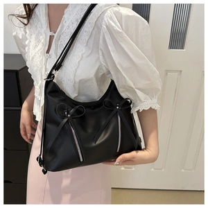 Detail of black leather hobo bag featuring satin bow accents and silver metal zippers