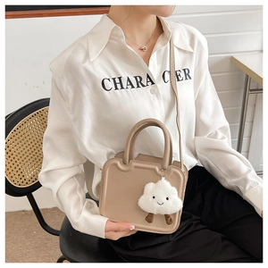 Detail of beige crossbody bag with plush cloud charm and integrated square handle