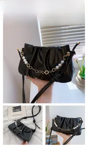 Detail of black pleated cloud bag featuring pearl chain and golden flower accents