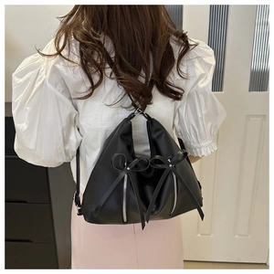 Detail of black backpack featuring decorative bows and dual silver metallic zippers