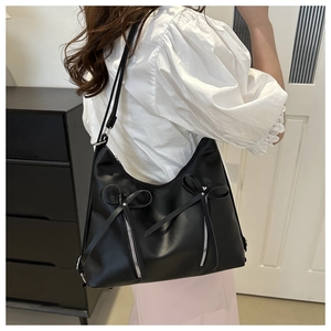 Détail du sac bandoulière noir avec nœuds décoratifs et fermetures éclair argentées