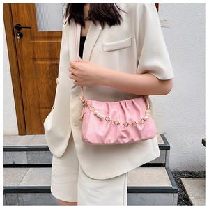 Detail of pink pleated underarm bag featuring pearl and golden flower chain on a model