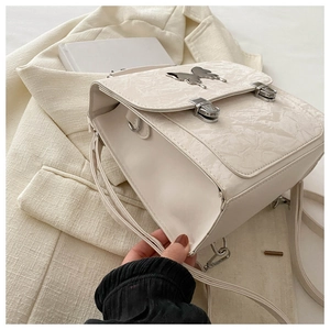 Detail of cream-white backpack featuring pleated texture and silver butterfly buckle closure