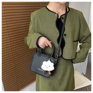 Detail of black wave-edge shoulder bag featuring a cute white plush cloud charm accessory
