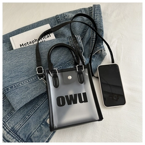 Détail du sac gelée en PVC transparent avec logo OWU noir et poignées en cuir sur tissu blanc