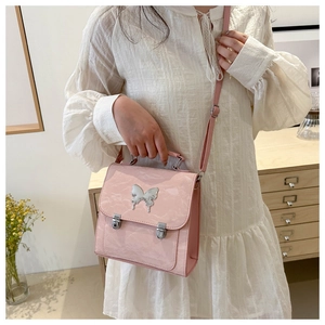 Close-up of pink shiny textured handbag with large silver butterfly buckle and crossbody strap