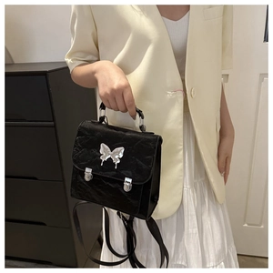 Detail of black pleated crossbody bag featuring a silver butterfly buckle and top handle