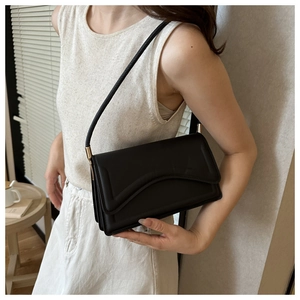 Close-up of black shoulder bag with curved flap detail and thin strap on a model