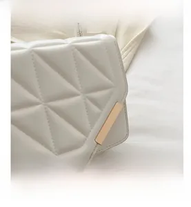 Detail of white quilted crossbody bag with golden metal trim and neat stitching