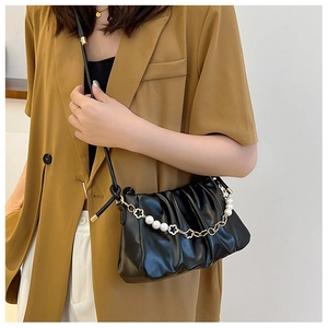 Detail of black pleated cloud bag with elegant pearl and gold flower chain strap