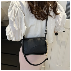 Détail du sac à bandoulière noir avec rabat ondulé et chaîne dorée sur la bandoulière