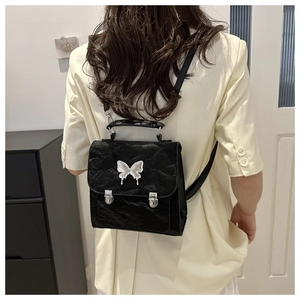 Detail of black Y2K backpack with silver butterfly buckle on model wearing white blazer