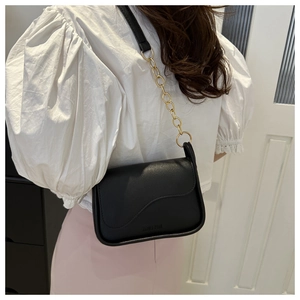 Detail of black leather crossbody bag with gold chain strap and decorative flap design