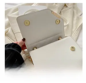 Detailed shot of gold magnetic hardware closure on white boxy crossbody flap bag