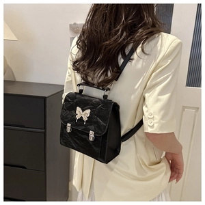 Detailed view of black pleated leather backpack with silver butterfly buckle on model