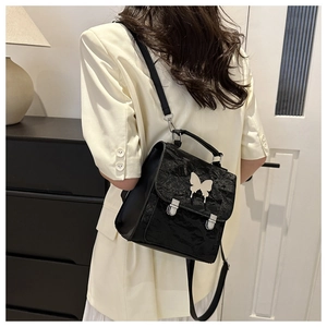 Detail of black pleated crossbody bag with silver butterfly charm and dual buckles