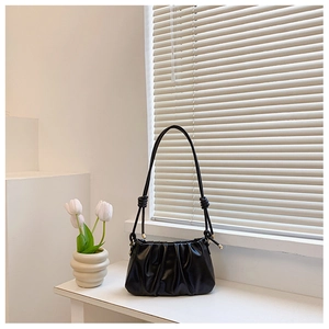 Detail of black pleated shoulder bag with sleek knotted strap and gold hardware accents