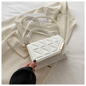 Detail of white quilted crossbody bag with gold trim and knotted handle on beige blazer