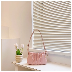 Close-up of pink pleated cloud bag with knotted handle and elegant gold metal accents