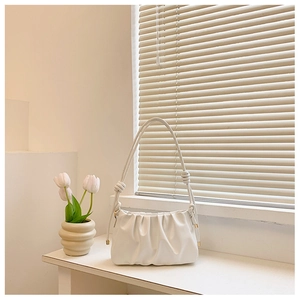 Detail of white pleated cloud bag with knotted strap on a bright minimalist desk