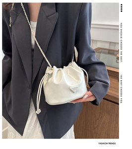 Detail of white drawstring bucket bag with litchi texture and metal chain strap