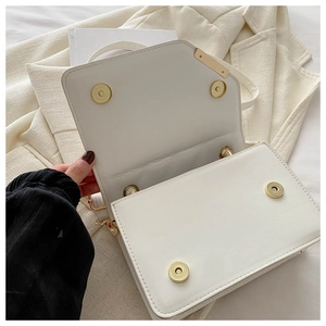 Detail view of white leather crossbody bag with gold magnetic snaps on beige blazer