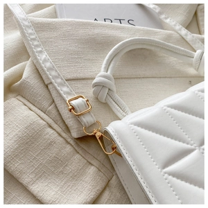 Close-up of white quilted crossbody bag with golden hardware and knotted top handle detail