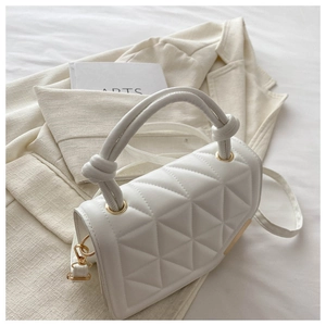 Close-up of white quilted handbag featuring golden clasp and knot handle detail