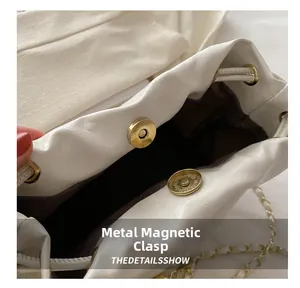 Detail of white drawstring bucket bag showing gold magnetic closure and chain strap