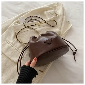 Detailed macro view of dark brown drawstring bucket bag with gold chain and triangle logo