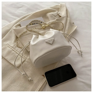 Detail view of cream drawstring bucket bag with gold chain strap and metal ball decoration