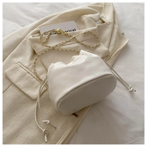 Close-up of cream drawstring bucket bag featuring a gold chain strap with adjustable metal ball