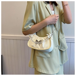Detail of cream pleated underarm bag featuring a bow charm and acrylic bead chain