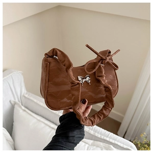 Detail view of brown pleated baguette bag with silver butterfly charm and scrunched handle