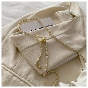 Close-up of golden metal chain with white leather weave and quilted ball detail