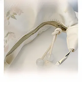 Close-up of pink floral embroidery and pearl bead zipper on beige oriental handbag